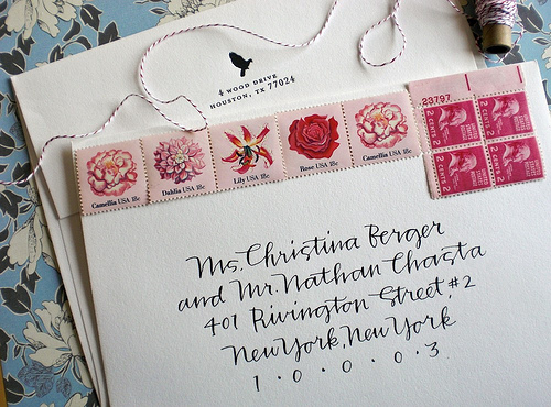 Beautiful handwritten calligraphy on an envelope that has stamps with flowers across the top of it.