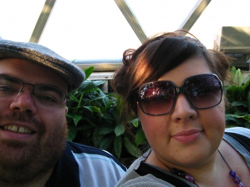 Photo of Natalie (wearing sunglasses) and half of Nick (wearing Pa's flatcap) inside the tropical dome of the Botanic Gardens 
