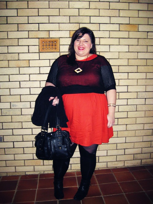 Photo of Natalie wearing a red babydoll dress with a mesh top, and black leggings. A jacket is slung over an arm that also carries a black purse.