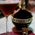 A photo of a bottle of Chambord with a French martini to the left of it. A fancy Chambord lid sits on a burgundy Chambord napkin.
