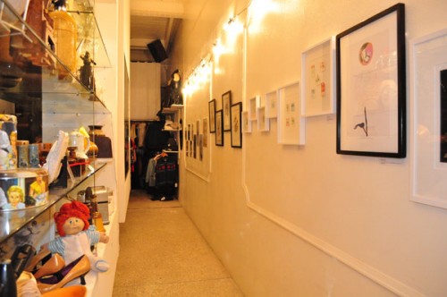 Photo of a wall on the right side of a narrow corridor with framed artworks. 