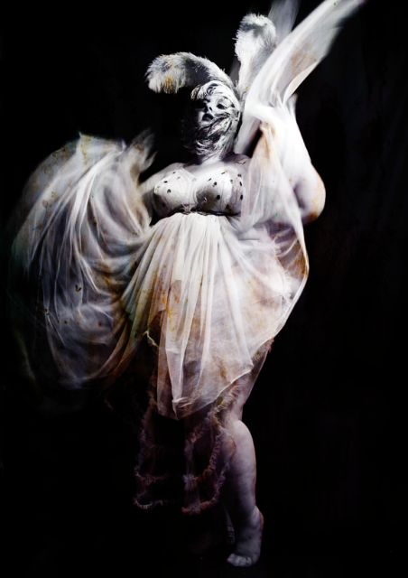 A photo of a pale skinned plus size woman in a white tulle-layered dress on a black background.