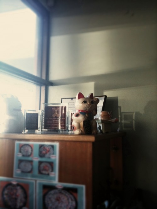 Waving cat in a sushi restaurant on top of a cabinet with certificates and a menu taped to the front of it.