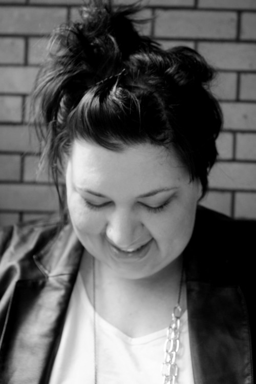 A black and white, head and shoulders, photo of me. I'm looking down, my hair is up, and I'm wearing a leather-look jacket with a white tshirt and a big chain necklace.