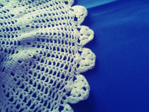 A photo of half a doily on a blue tablecloth.