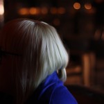 A blonde woman is on the left with out of focus ambient light to her right.