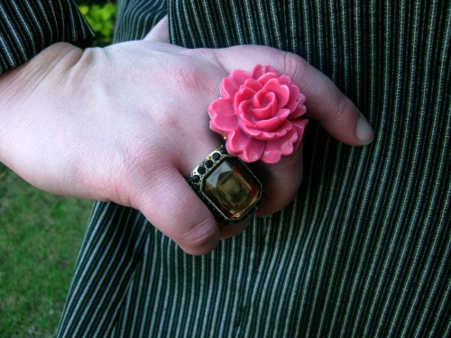 Photograph of Natalie's right hand, she wears two large rings: one a 3D pink flower, the other an amber rectangular gem.