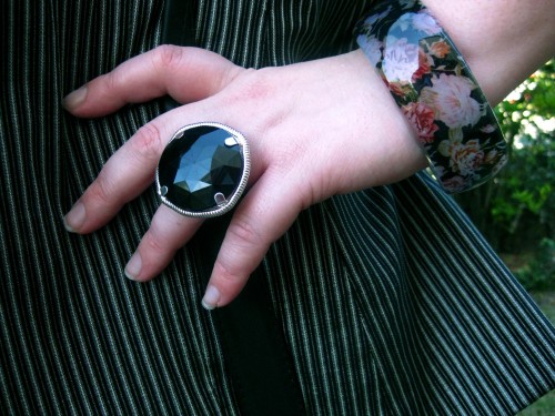 Photograph of Natalie's left hand, she wears a huge round black faceted gem ring and a plastic bangle with a floral print trapped inside.