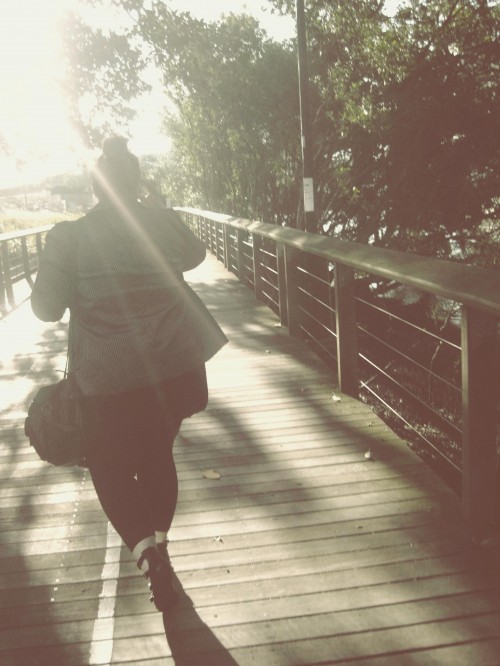 An overly edited photo of Natalie walking away down a wooden walkway, a sunflare blowing out most of the top third of the picture.