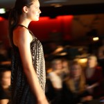 Profile of a model walking down the runway in a floaty dress in a dark small pattern.