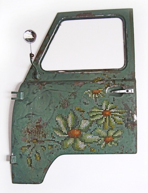 The door of a truck, teal in colour but rusted, has been embellished with large cross stitched flowers.