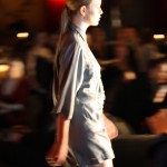 Side profile of a model walking in a grey romper-style design - with bracelet length sleeves and short shorts.
