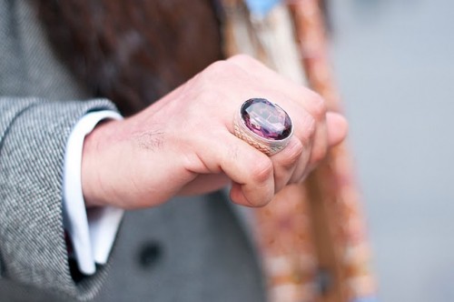 A close up of a man's hand wearing a spectacularly huge purply coloured gem ring. 
