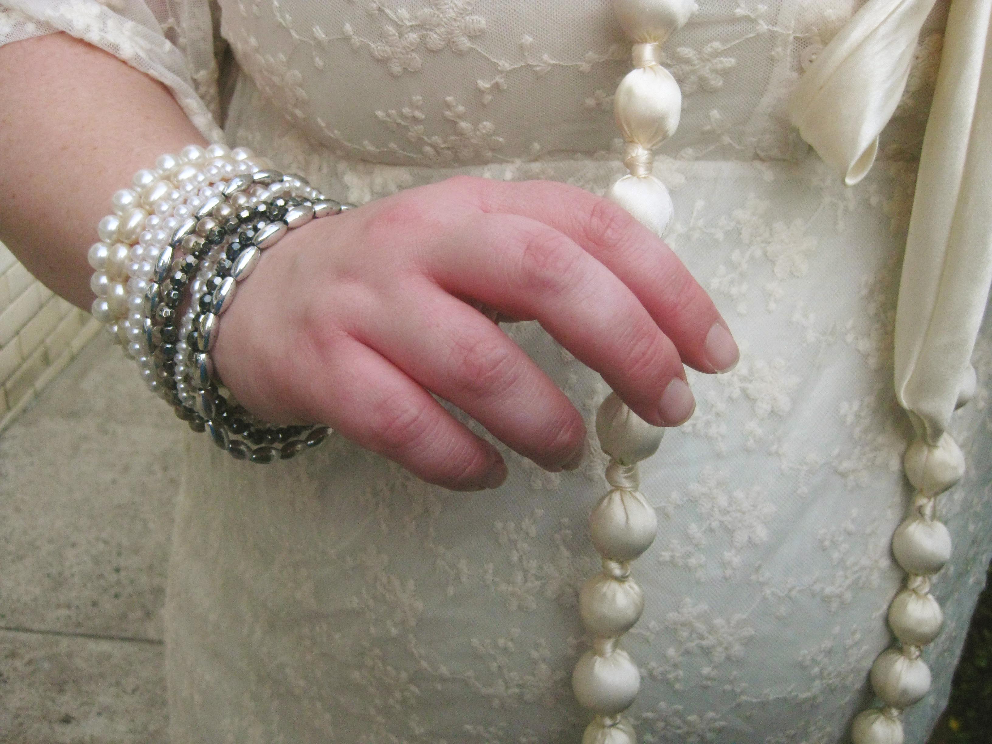 A photo of my right hand (with lots of bracelets) lightly clasping a very long cream bead necklace.
