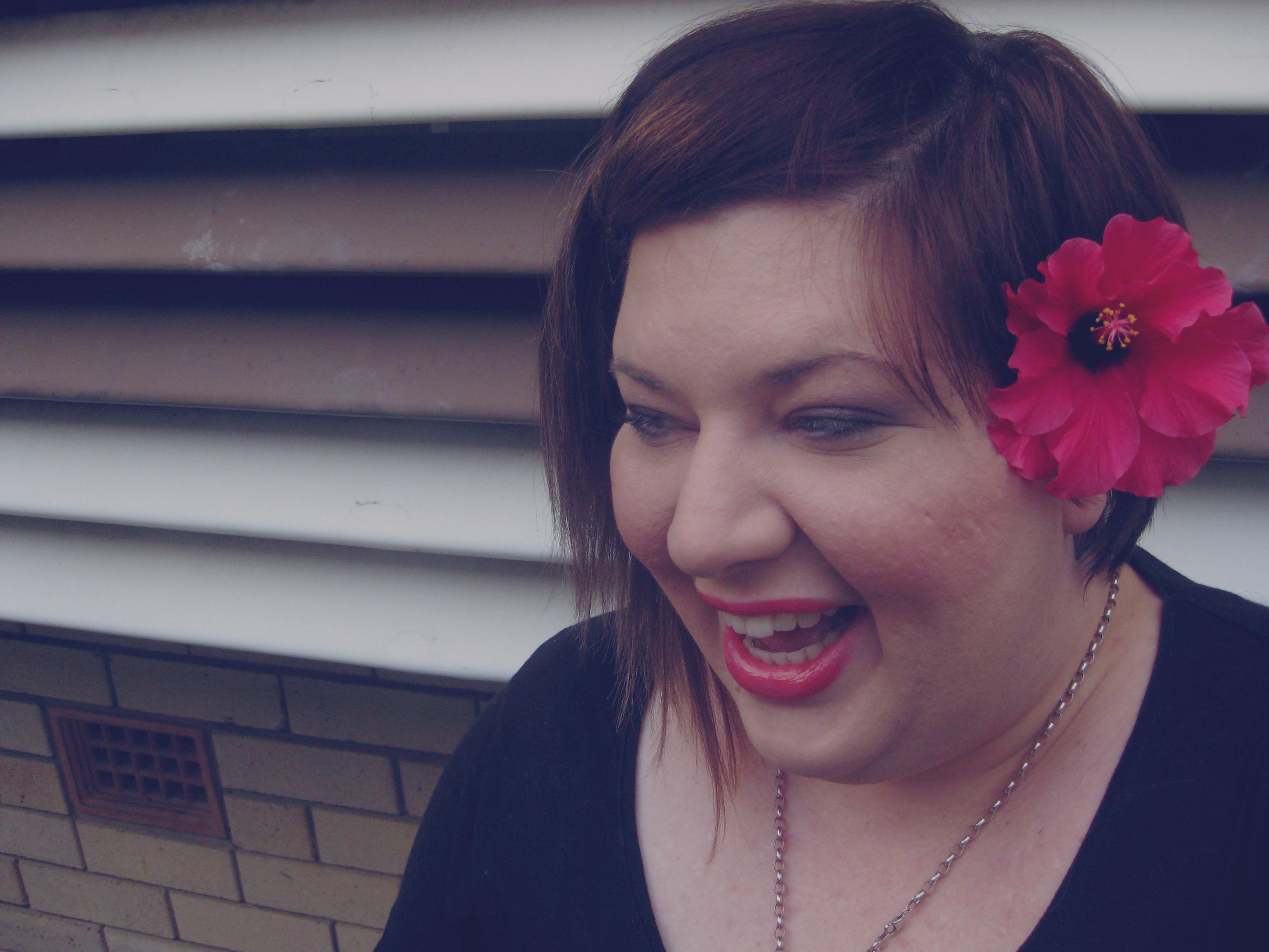 Photo of me laughing with a red hibiscus tucked behind my ear.