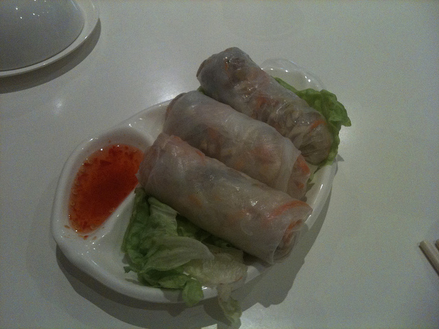 Photo of three rice paper rolls on a bed of green lettuce with some sweet chilli sauce.