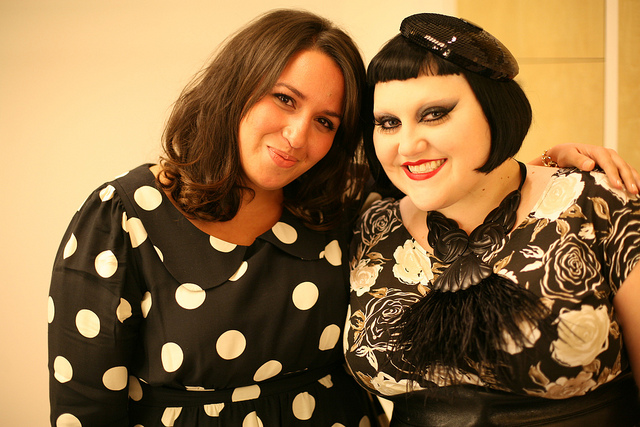 Photo of Sakina wearing the polka dot dress with Beth Ditto, who wears the floral dres with a feathered statement necklace and a small sequinned beret like headpiece.