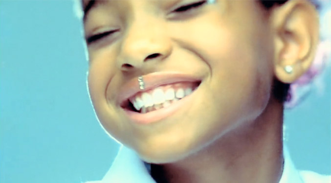 Still from Willow Smith's Whip My Hair Video: close up on Willow smiling. She's got some little rhinestones stuck down the middle of her top lip.