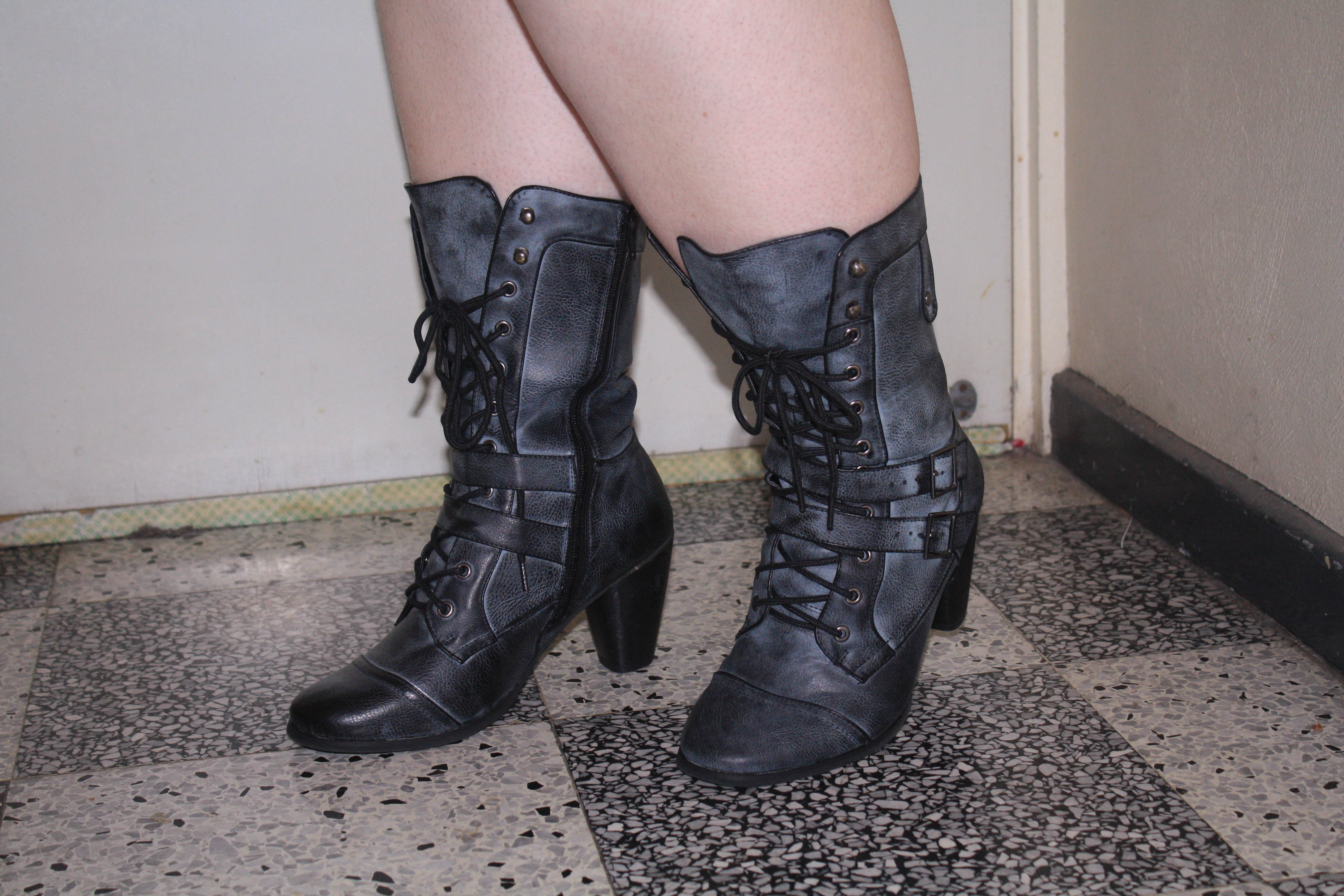 Photo of my feet and calves shod in black and grey distressed looking witchy boots. They lace up and have two tabs that reach across the foot and buckle on the other side.