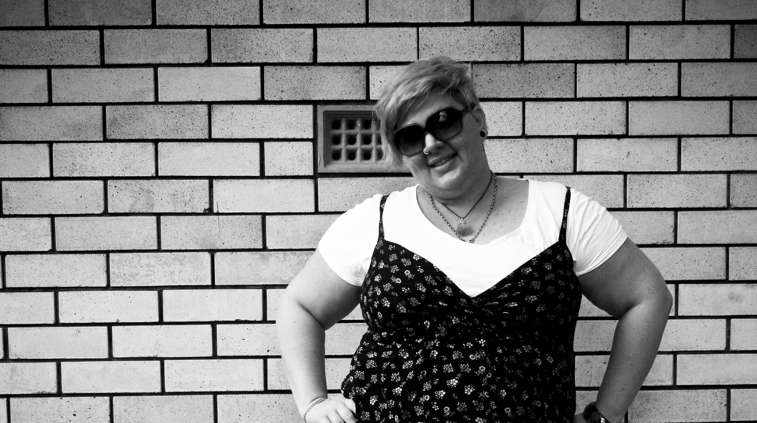 Photo of me standing against a brick wall, hands on hips and smiling.