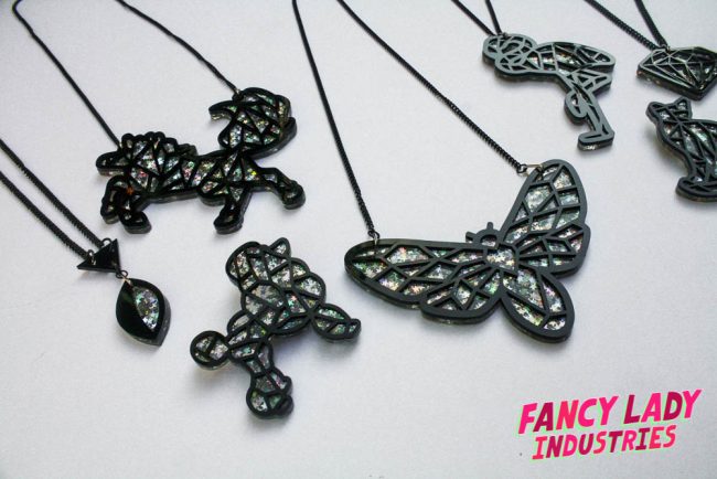 Some of my unicorn, moth and flamingo necklaces with a poodle brooch, all made from laser cut black and silver holographic glitter acrylic available on Fancy Lady Industries.