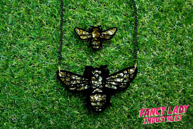 A Teddy Bear Bee necklace and brooch set made out of laser cut black and gold glitter acrylic, available on Fancy Lady Industries