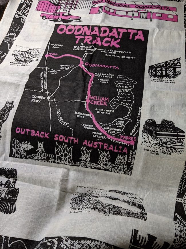 A tea towel screenprinted with the Oodnadatta track in black with hot pink highlights.